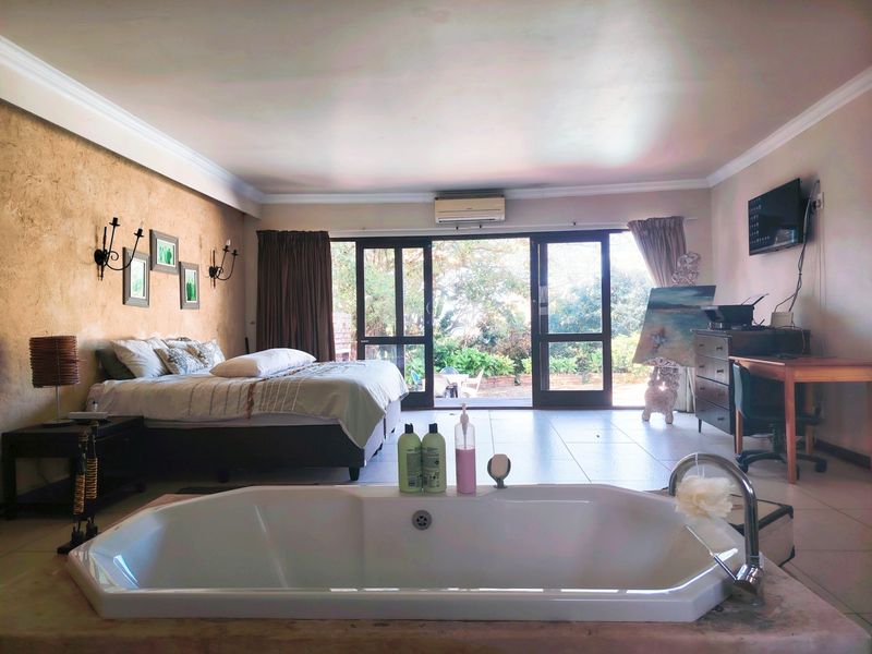 Spacious bedroom featuring an integrated bathtub, tiled flooring, and sliding glass doors opening to a garden view.