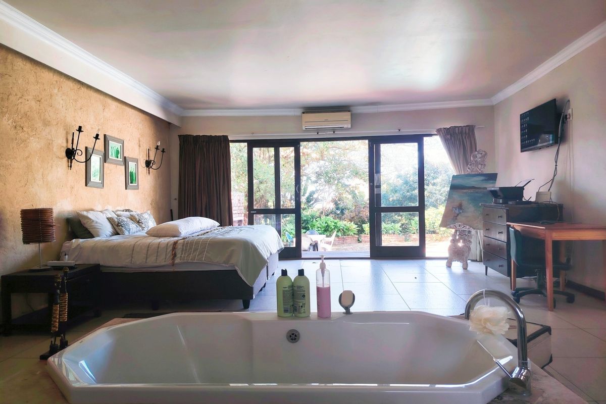 Spacious bedroom featuring an integrated bathtub, tiled flooring, and sliding glass doors opening to a garden view.