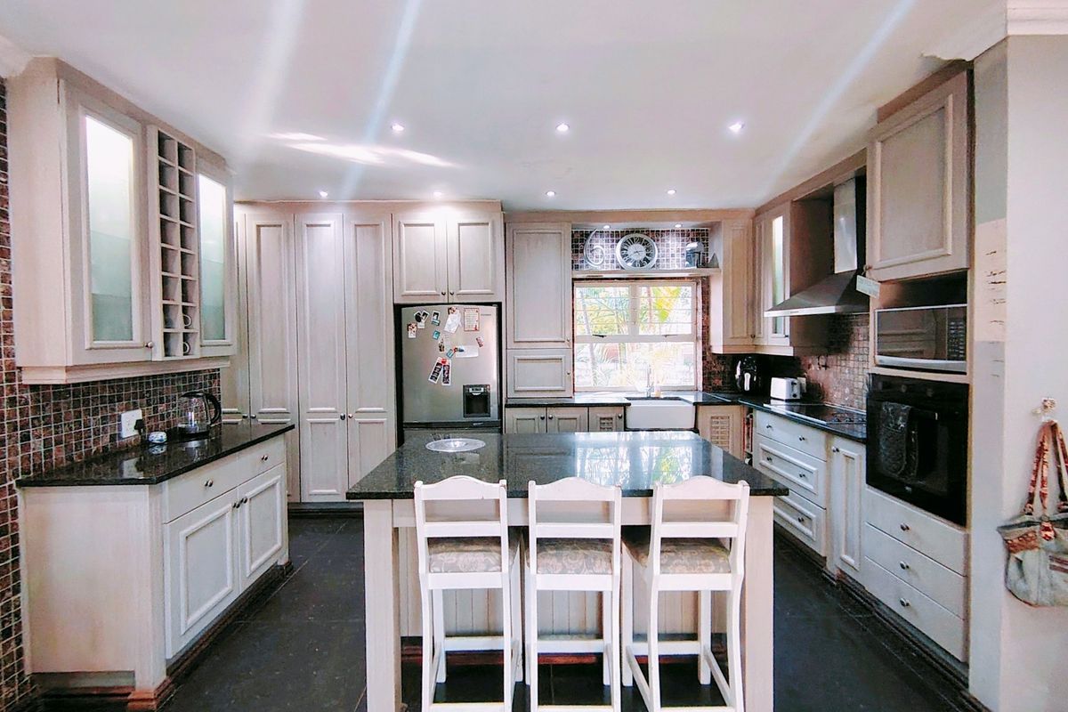 A well-appointed kitchen featuring a central island with granite countertops, built-in oven, microwave, extractor fan, and classic cabinetry with a farmhouse sink.