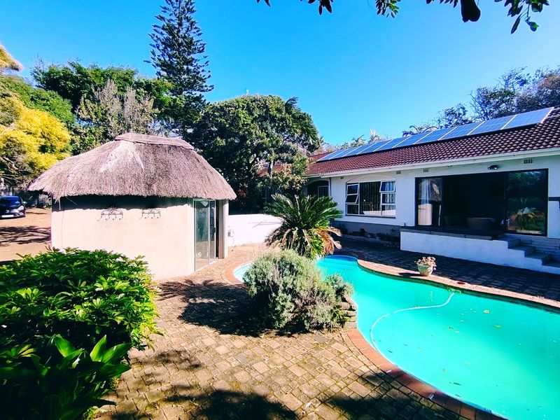 Outdoor pool area featuring a swimming pool, paved patio, and a traditional thatch lapa, complemented by roof-mounted solar panels.