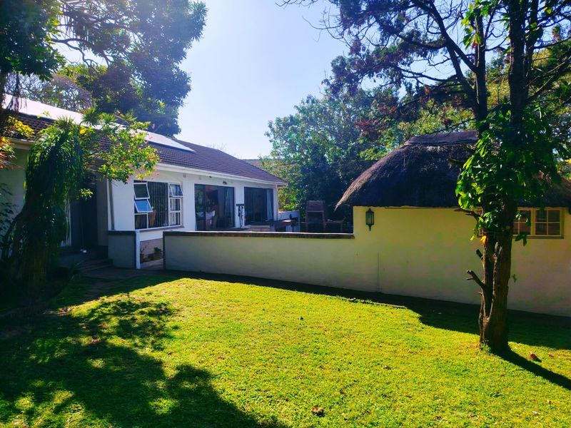 Rear view of the property featuring a landscaped garden, a main house with solar panels, and a separate structure with a traditional thatched roof.