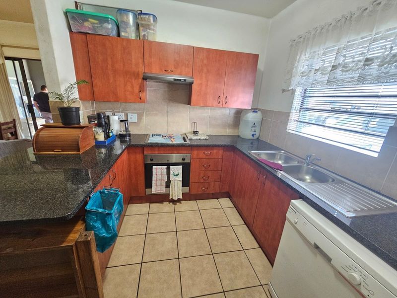 Functional kitchen featuring wood-finish cabinetry, granite countertops, built-in oven with extractor fan, and tiled flooring, offering a practical layout for daily use.