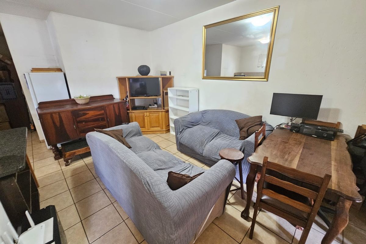 A living area featuring ceramic floor tiles and a wall-mounted mirror, offering a functional space with potential for cosmetic updates and modernization.