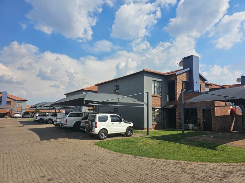 Exterior view of a multi-unit commercial or residential complex featuring brick and rendered facades, tiled roofing, and dedicated shade cloth parking bays.