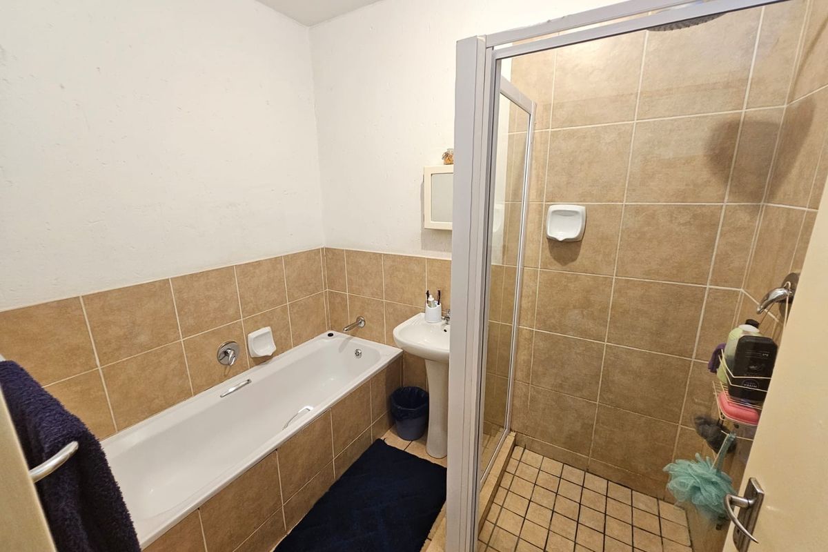 A functional bathroom featuring a separate bathtub and shower enclosure with neutral wall tiling and a pedestal basin.