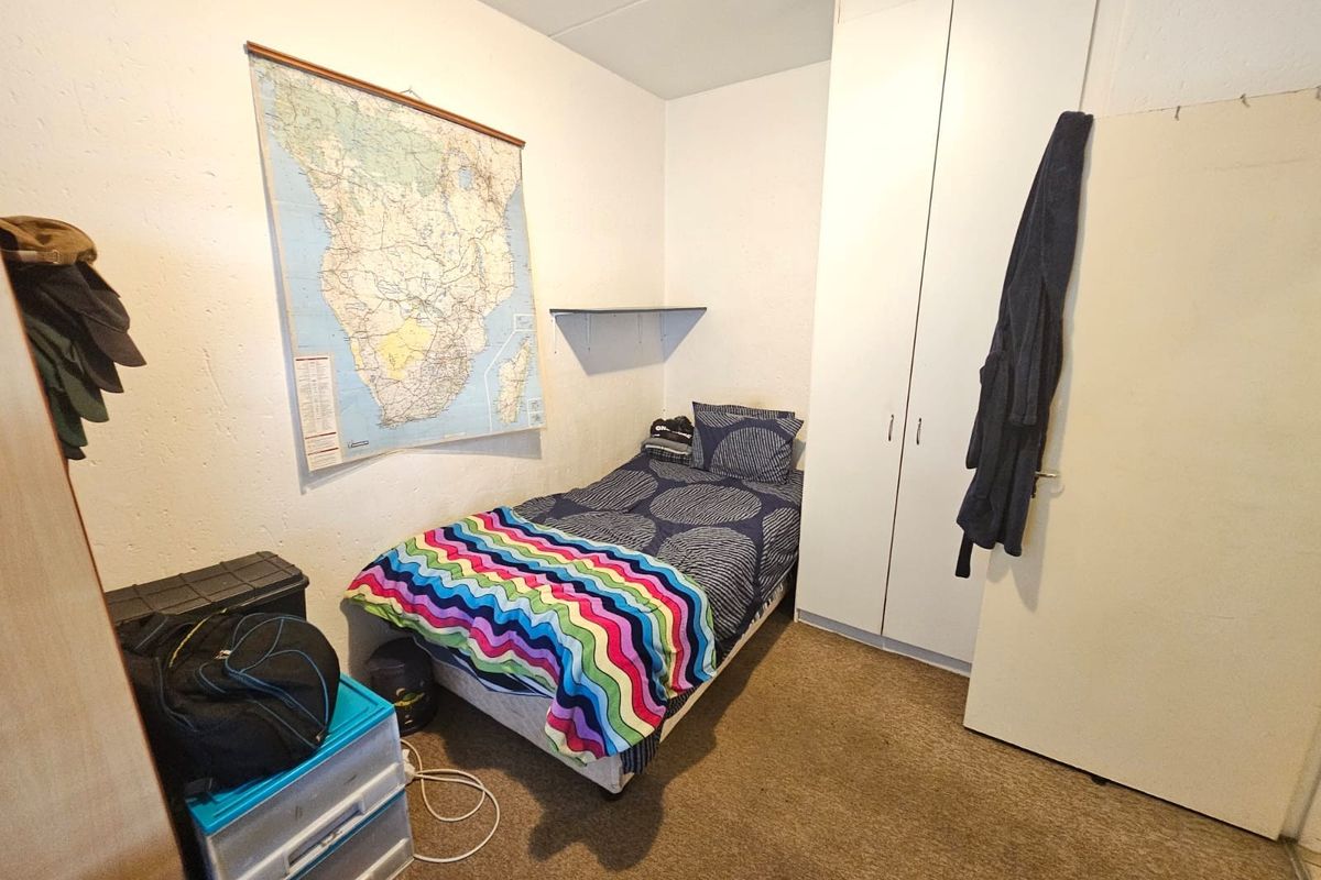 A functional bedroom featuring a built-in wardrobe and a wall-mounted shelf, providing essential storage space within a compact layout.