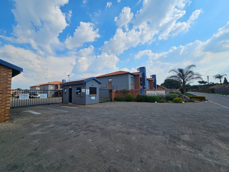 Front entrance view of Avion Mews complex featuring a secure gated access point, guard house, and paved driveway area.