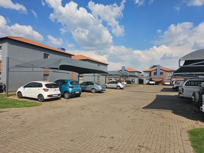 A well-maintained commercial parking area featuring paved surfaces and multiple shade cloth carports serving the adjacent multi-story brick buildings.
