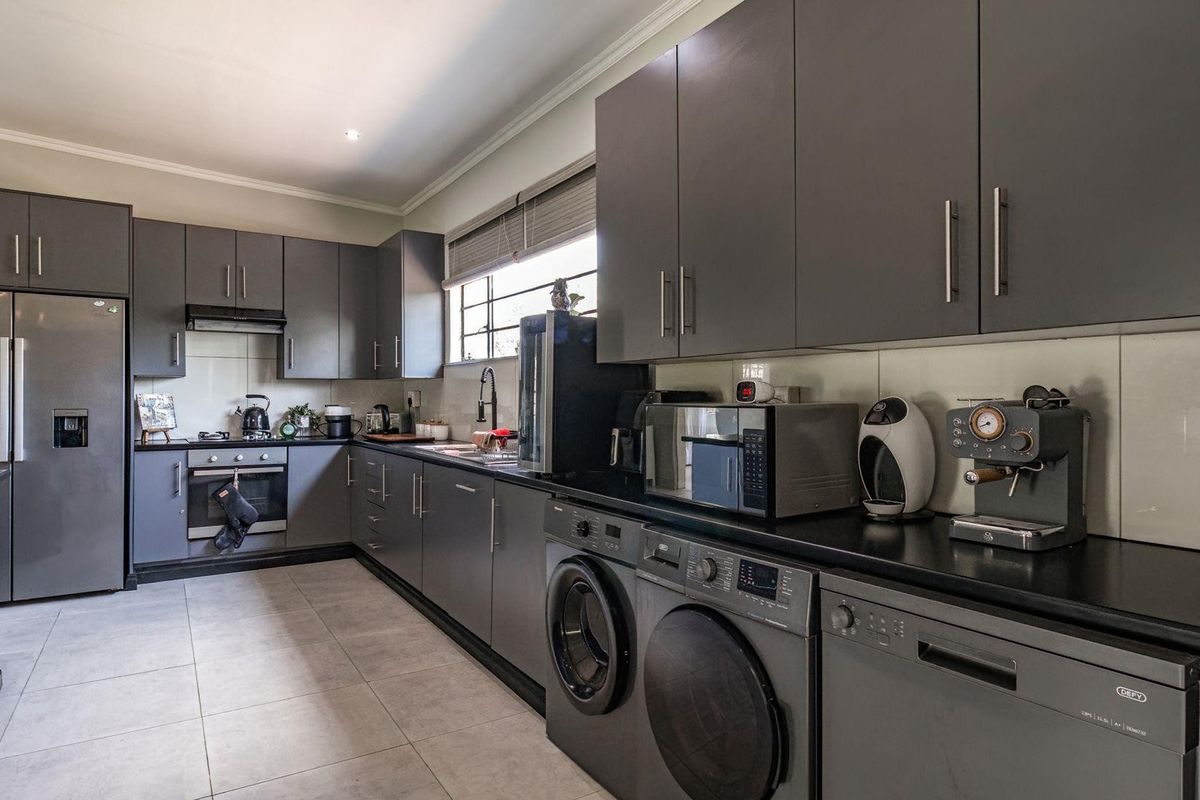 Modern kitchen featuring dark grey cabinetry, stone countertops, integrated appliances, and tiled flooring, offering a sleek and functional workspace.