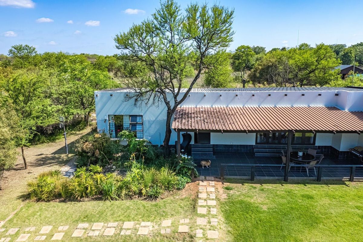 Aerial view of the rear exterior featuring a covered patio, tiled flooring, and a stone pathway leading into the landscaped garden area.
