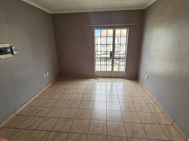 An empty living room featuring neutral tiled flooring and a glass-paneled door providing natural light and access to the exterior.