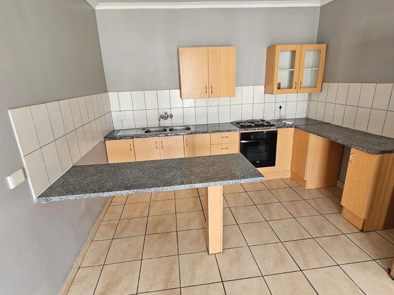 A functional kitchen featuring laminate cabinetry, granite countertops, a built-in oven, gas hob, and a convenient breakfast bar with tiled flooring.