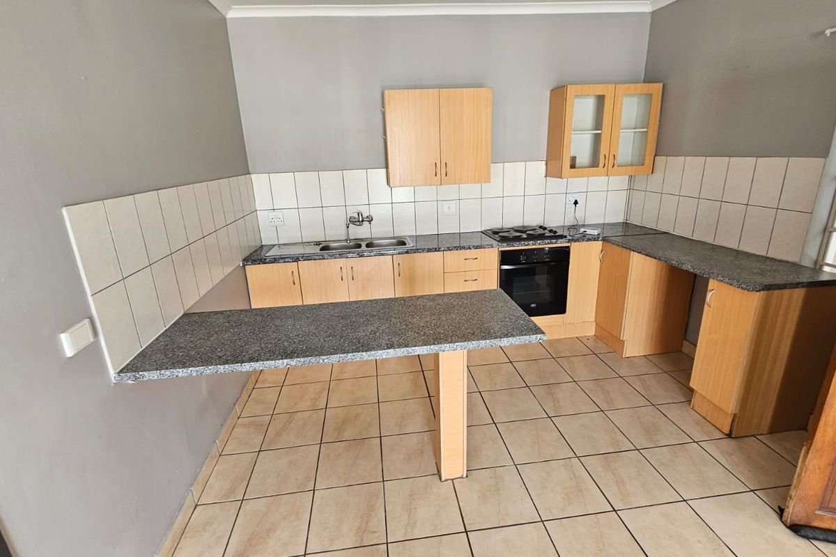 A functional kitchen featuring laminate cabinetry, granite countertops, a built-in oven, gas hob, and a convenient breakfast bar with tiled flooring.