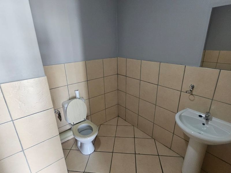 A functional bathroom featuring a pedestal washbasin, toilet, and neutral ceramic tiling on both walls and floors.