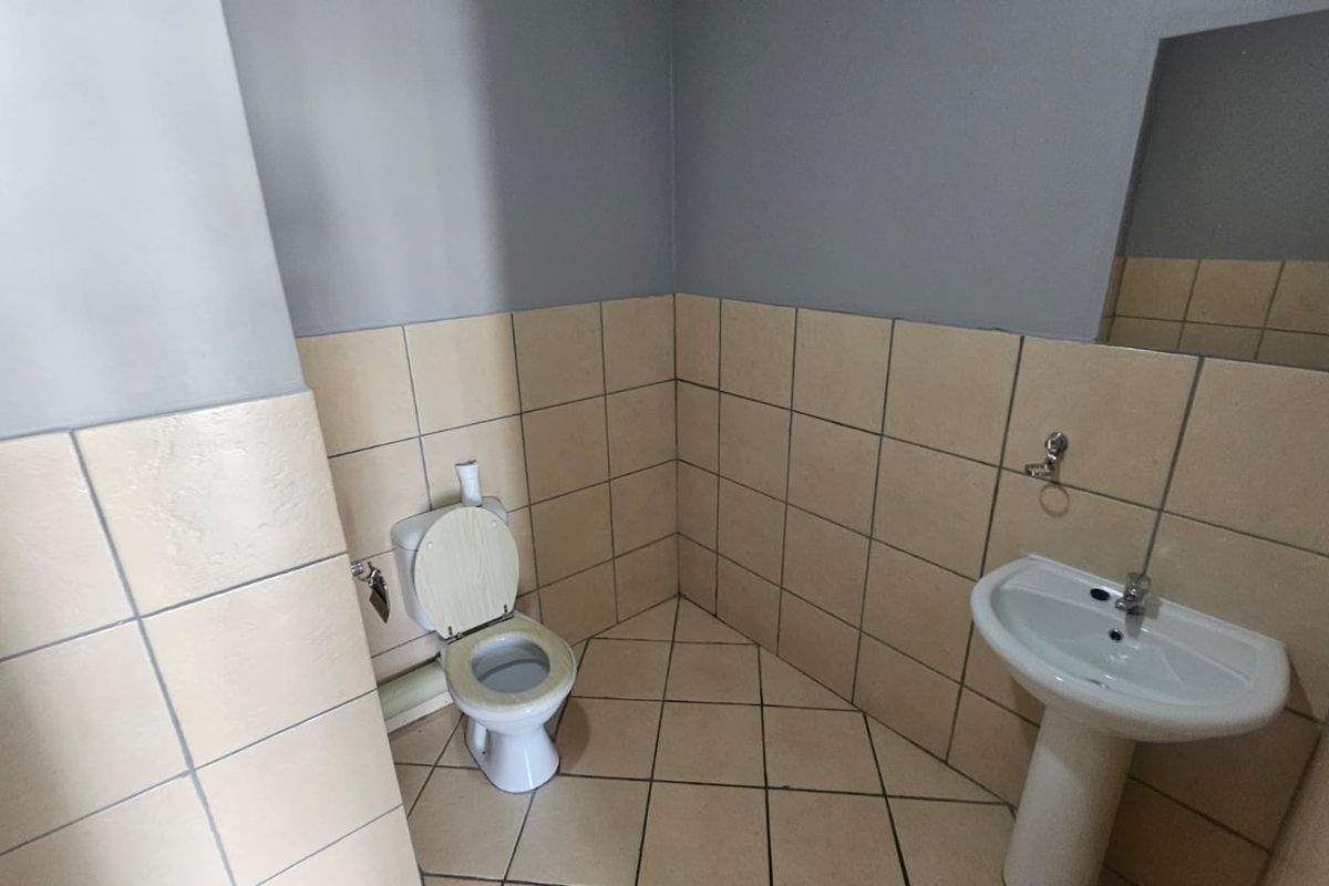 A functional bathroom featuring a pedestal washbasin, toilet, and neutral ceramic tiling on both walls and floors.
