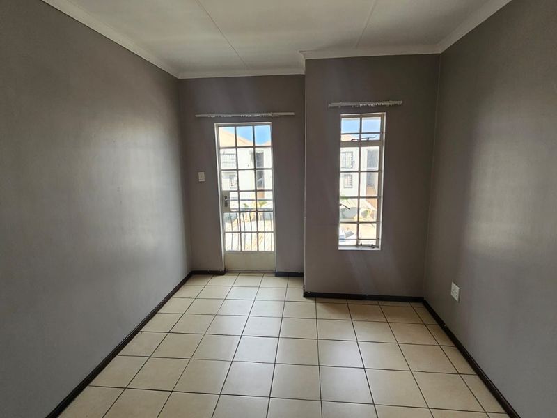 An empty living room featuring neutral grey walls, tiled flooring, and access to an exterior area through a security-fitted door.