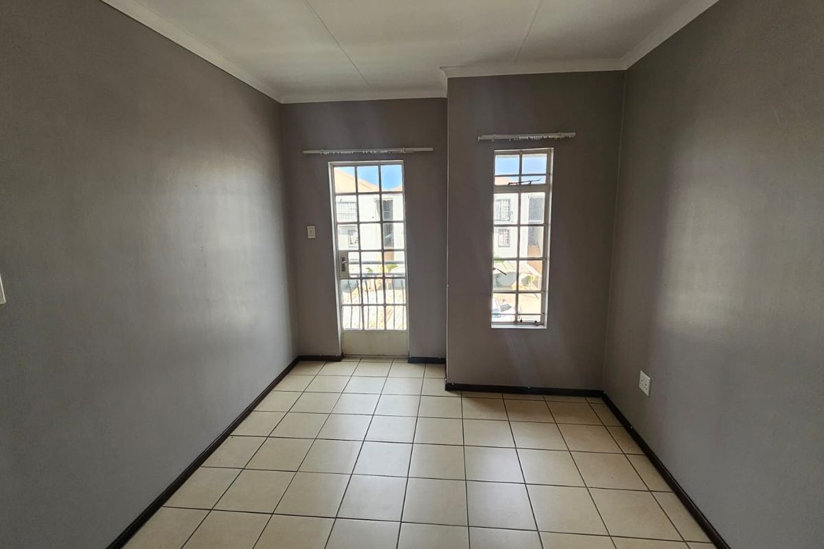An empty living room featuring neutral grey walls, tiled flooring, and access to an exterior area through a security-fitted door.