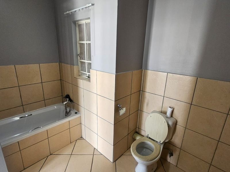 A functional bathroom featuring a bathtub, toilet, and neutral wall and floor tiling, offering a blank canvas for potential cosmetic updates.