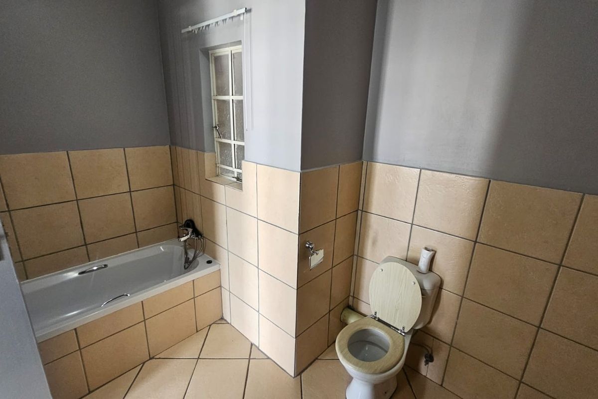 A functional bathroom featuring a bathtub, toilet, and neutral wall and floor tiling, offering a blank canvas for potential cosmetic updates.