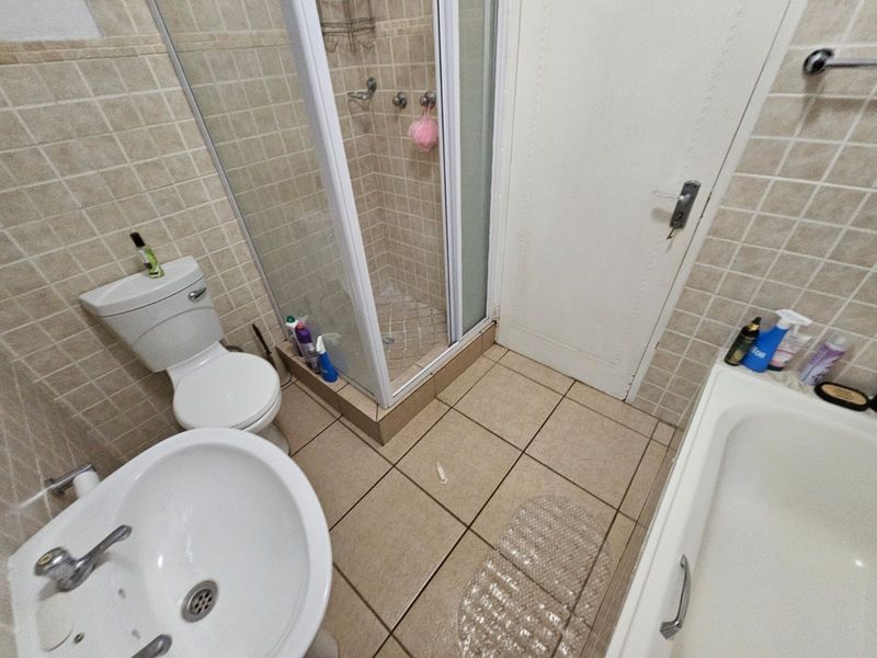 A functional bathroom featuring a shower enclosure, bathtub, pedestal basin, and toilet, finished with neutral ceramic wall and floor tiles.