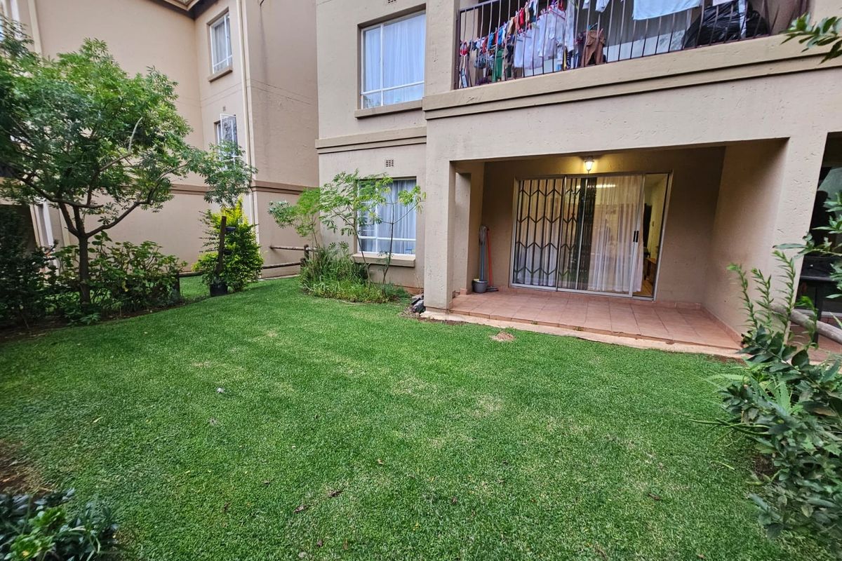 Rear view of the townhouse featuring a private garden, a covered tiled patio, and an upper-level balcony with metal railings.