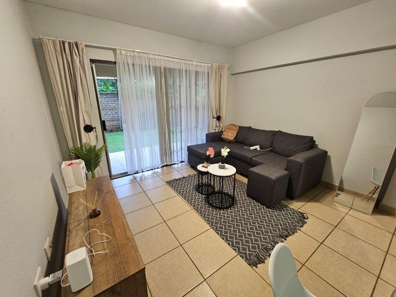A living room featuring neutral tiled flooring and a sliding glass door that provides direct access to the outdoor patio area.