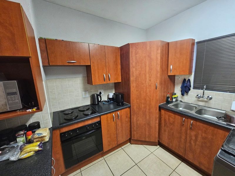 Functional kitchen featuring wood-finish cabinetry, dark laminate countertops, built-in oven and hob, double sink, and tiled flooring with a neutral backsplash.