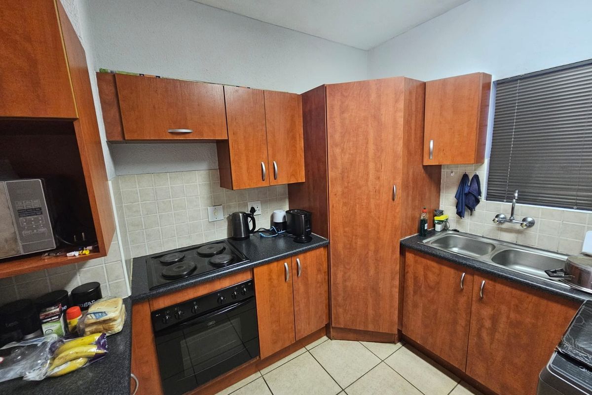 Functional kitchen featuring wood-finish cabinetry, dark laminate countertops, built-in oven and hob, double sink, and tiled flooring with a neutral backsplash.