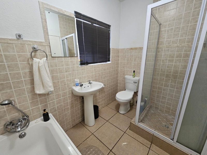 A functional bathroom featuring a pedestal basin, toilet, separate shower enclosure, and a bathtub with tiled wall and floor finishes.