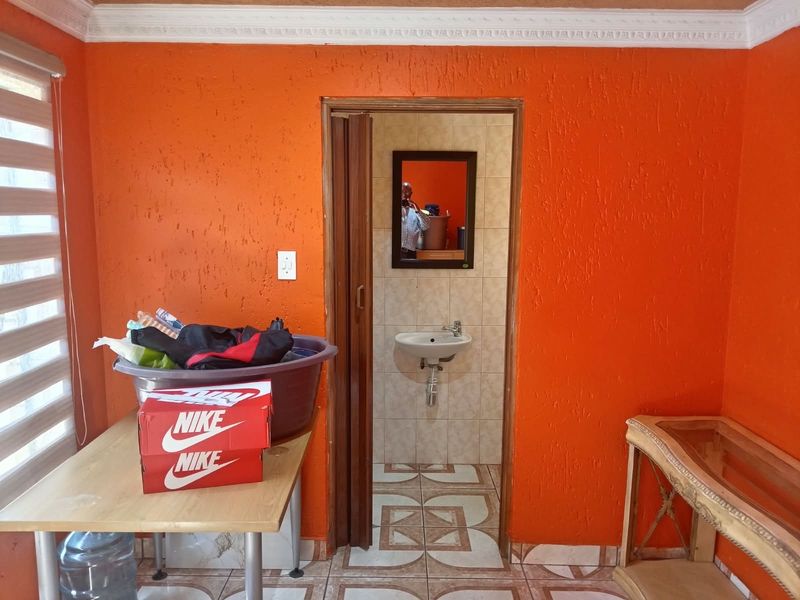 A small bathroom featuring a wall-mounted basin, tiled walls and floors, and a folding door entrance, requiring cosmetic updates to the wall finishes.