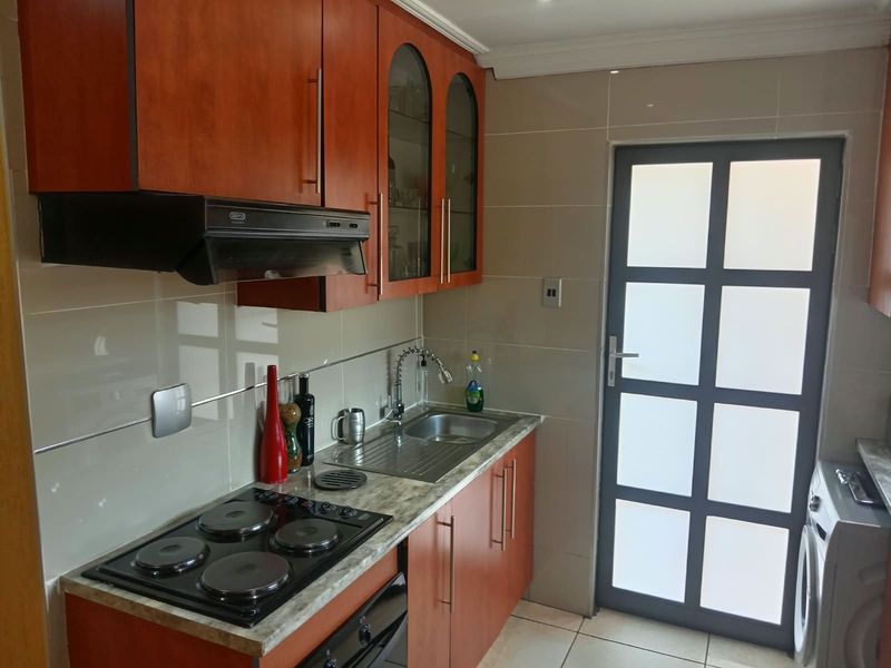A functional kitchen featuring wood-finish cabinetry, a built-in electric hob with extractor fan, stainless steel sink, and a modern frosted glass exterior door.