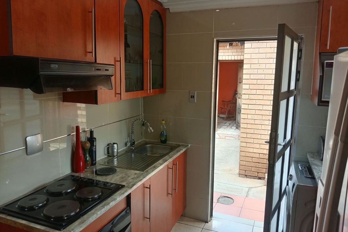 Compact kitchen featuring wooden cabinetry, laminate countertops, built-in electric hob with extractor fan, and direct access to an outdoor courtyard area.