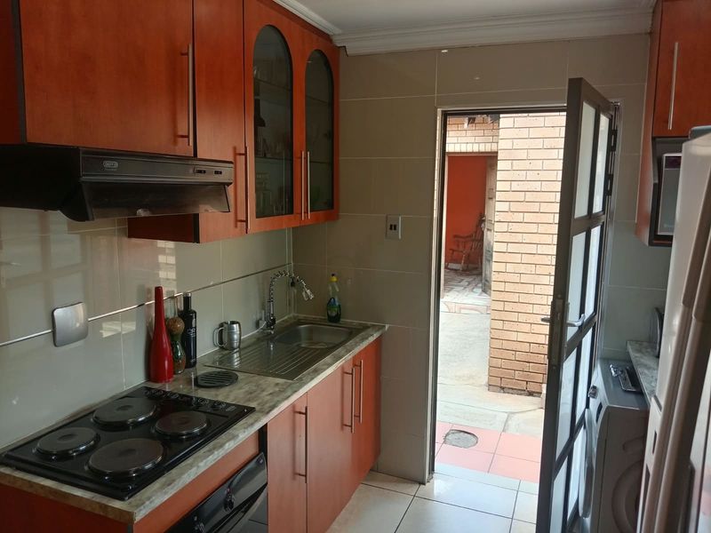 Compact kitchen featuring wooden cabinetry, laminate countertops, built-in electric hob with extractor fan, and direct access to an outdoor courtyard area.