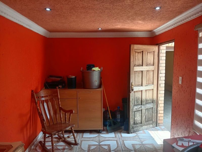 A utility space featuring textured orange walls, recessed ceiling lighting, decorative cornice, and ceramic floor tiles with a wooden door leading to an adjacent area.