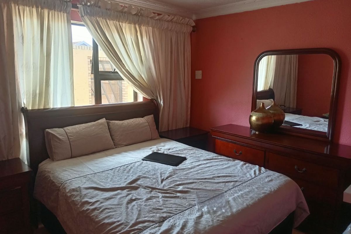A standard bedroom featuring tiled flooring, cornice detailing, and an aluminium-framed window, providing a functional and lived-in space.
