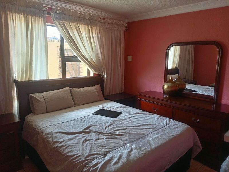 A standard bedroom featuring tiled flooring, cornice detailing, and an aluminium-framed window, providing a functional and lived-in space.