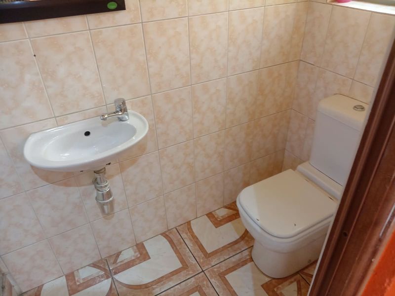 A compact guest bathroom featuring a wall-mounted basin, chrome faucet, and standard toilet with neutral ceramic wall and floor tiling.