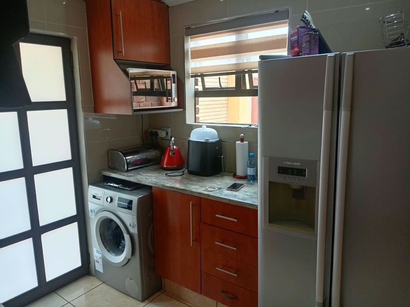 A functional laundry area featuring built-in cabinetry, tiled splashbacks, and space for a washing machine and large refrigerator.