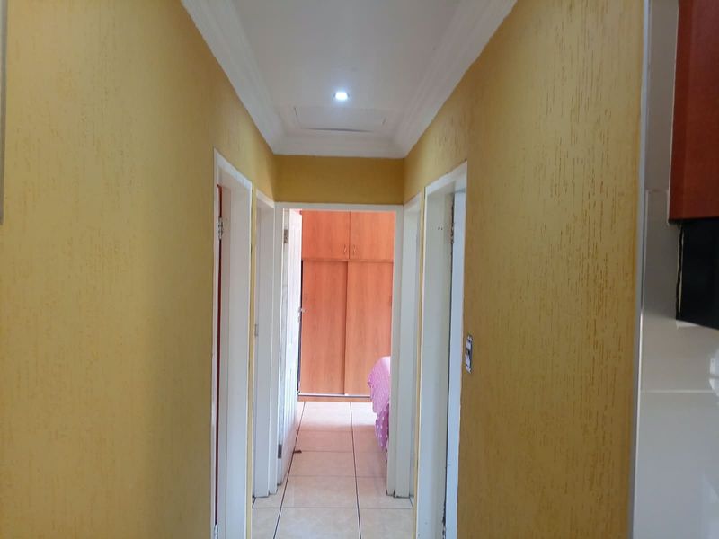 A functional hallway featuring textured yellow walls, tiled flooring, and recessed ceiling lighting, providing access to adjacent rooms and built-in bedroom storage.