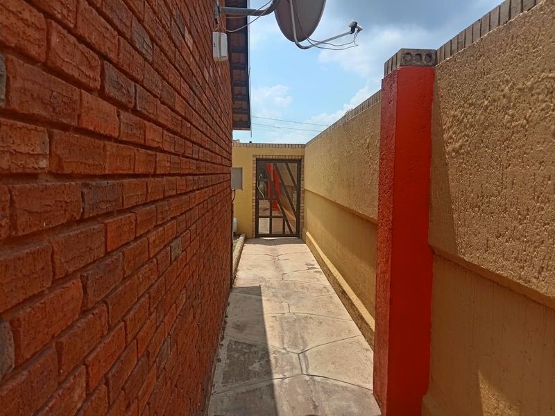A narrow side passage featuring a brick wall, paved walkway, and a secure metal gate leading to the rear outdoor area.