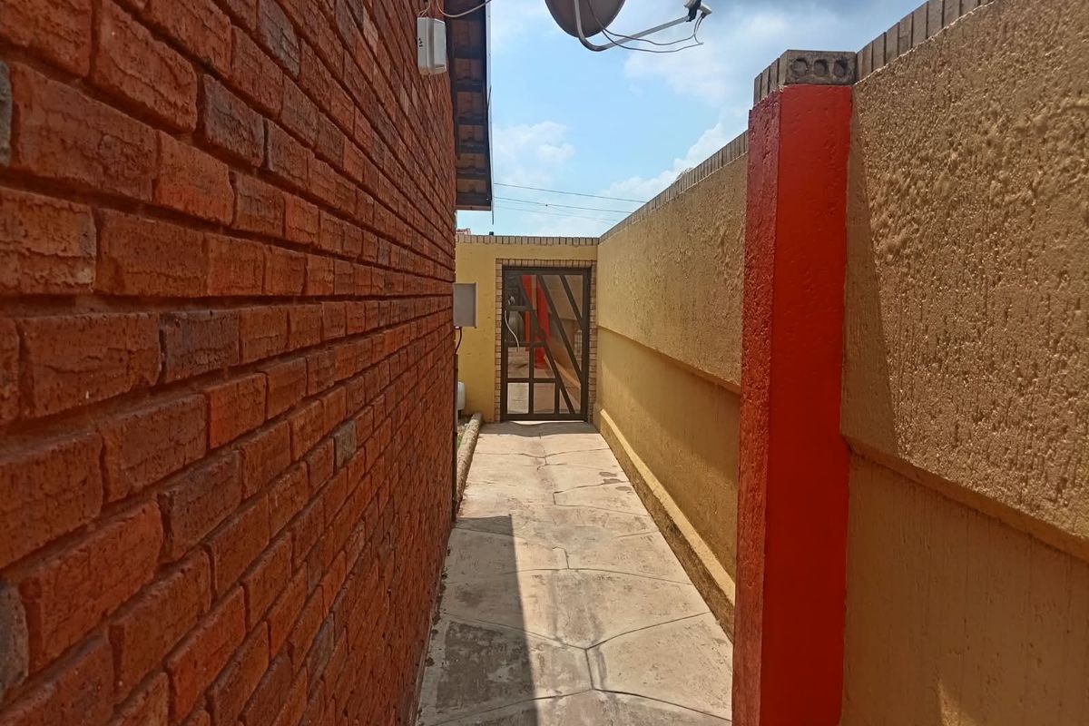 A narrow side passage featuring a brick wall, paved walkway, and a secure metal gate leading to the rear outdoor area.