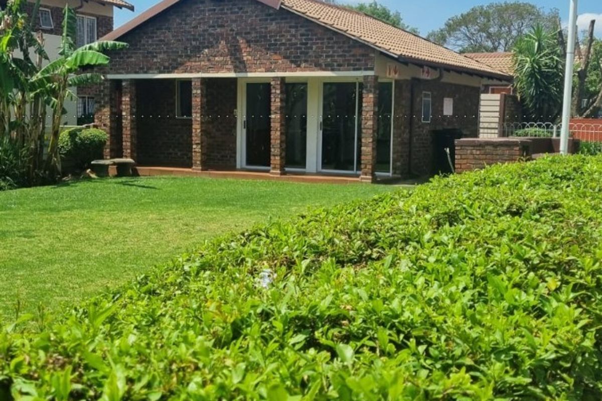 A well-maintained face brick apartment unit featuring a covered patio, sliding glass doors, and a neat garden area.