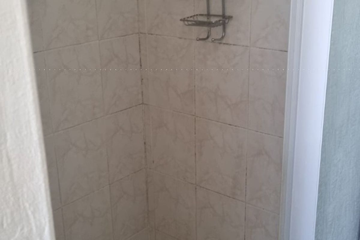 A compact shower stall featuring tiled walls and flooring, requiring some maintenance and cosmetic updates to refresh the space.