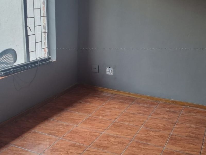 An empty bedroom featuring tiled flooring, grey painted walls, and a window fitted with security bars.
