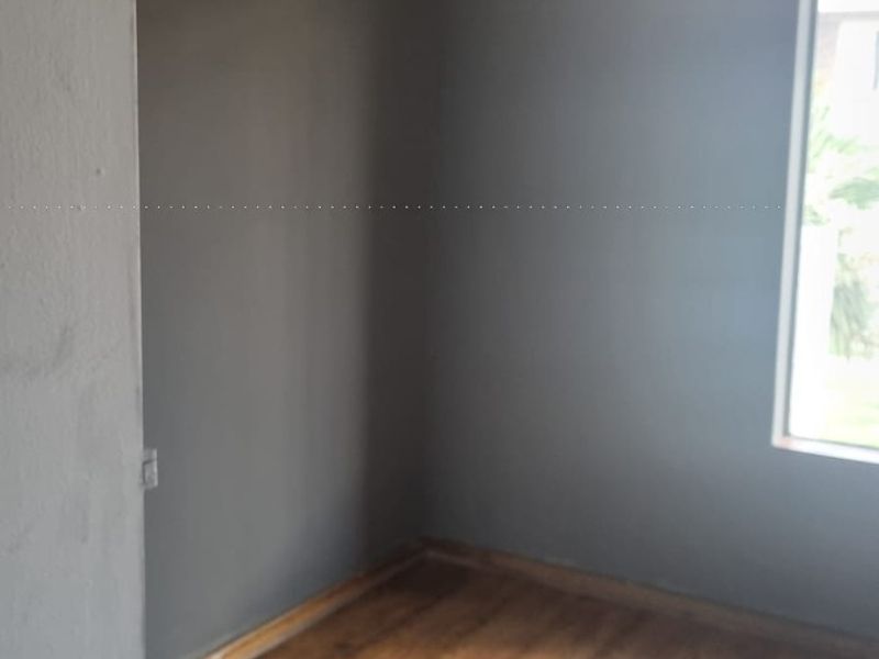 An empty bedroom featuring dark grey walls, laminate wood flooring, and white cove cornicing, awaiting personal touches and furniture.