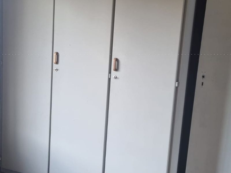 A bedroom featuring built-in cupboards and laminate flooring, offering a functional storage solution in a neutral space.