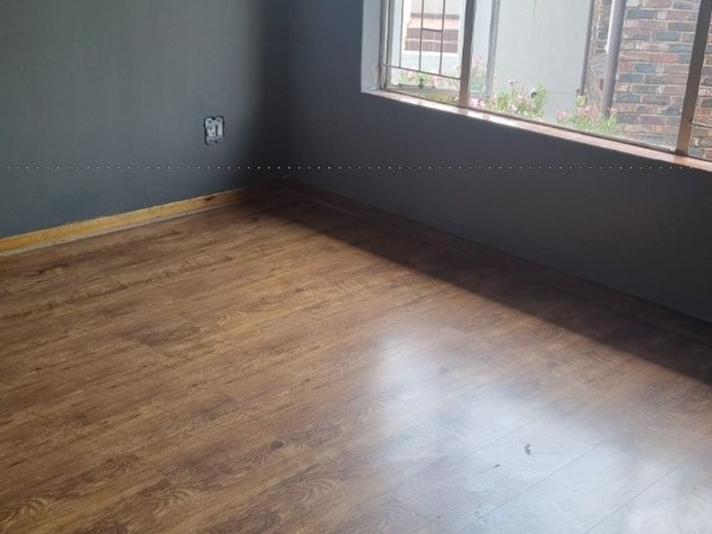 An empty bedroom featuring laminate flooring, dark grey walls, and a window fitted with security bars.
