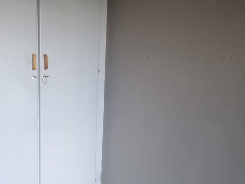 A clean, empty bedroom featuring laminate flooring and a built-in cupboard with a neutral grey wall finish.
