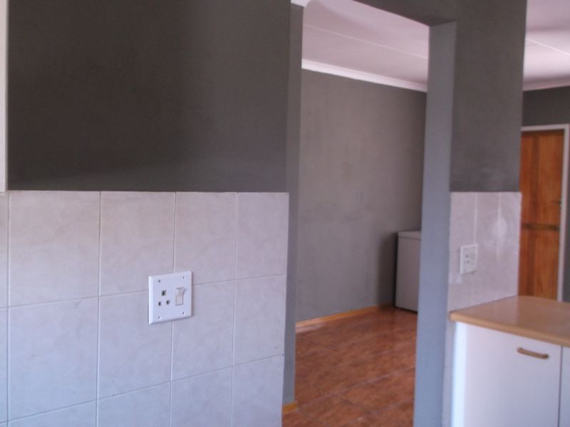 Open plan living area featuring tiled splashbacks, neutral grey walls, and tiled flooring, providing a versatile space for kitchen and living arrangements.