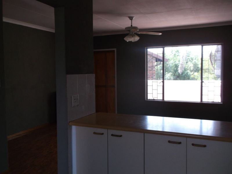 An open-plan living and kitchen area featuring built-in cabinetry, a ceiling fan, and large windows with security bars.